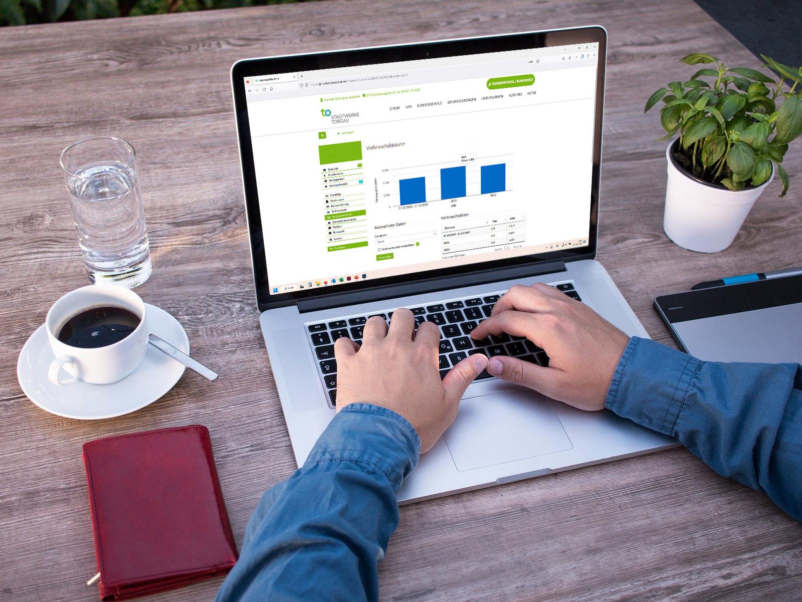 Notebook mit Login-Bereich des Kundenportals auf Schreibtisch mit Kaffee und Smartphone