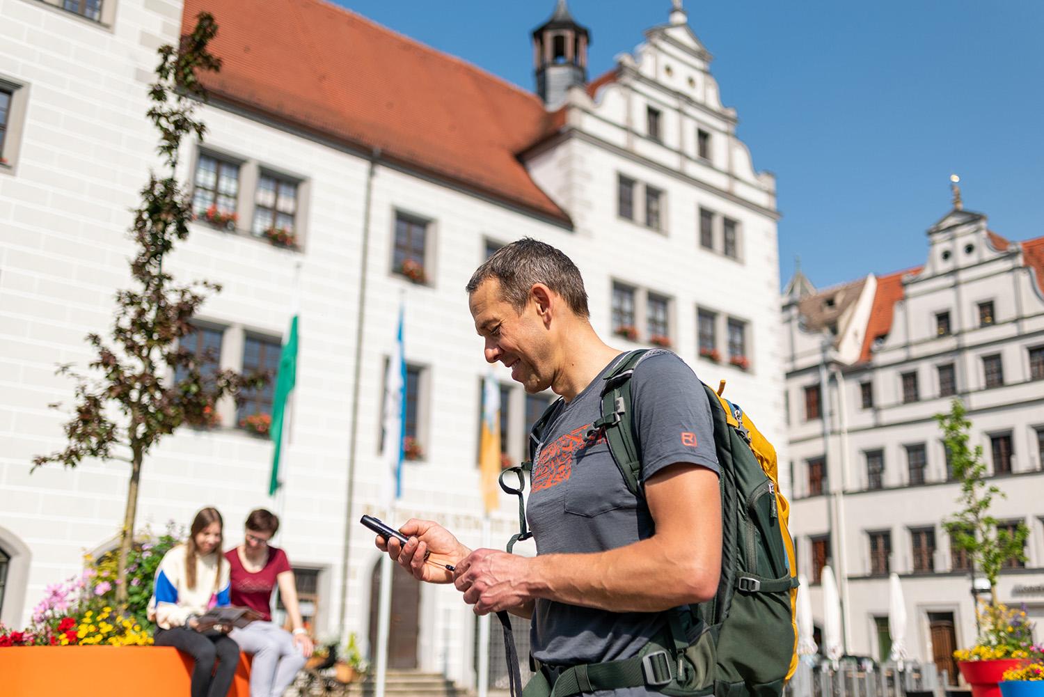 Mann hält vor dem Rathaus in Torgau einen Audioguide in der Hand