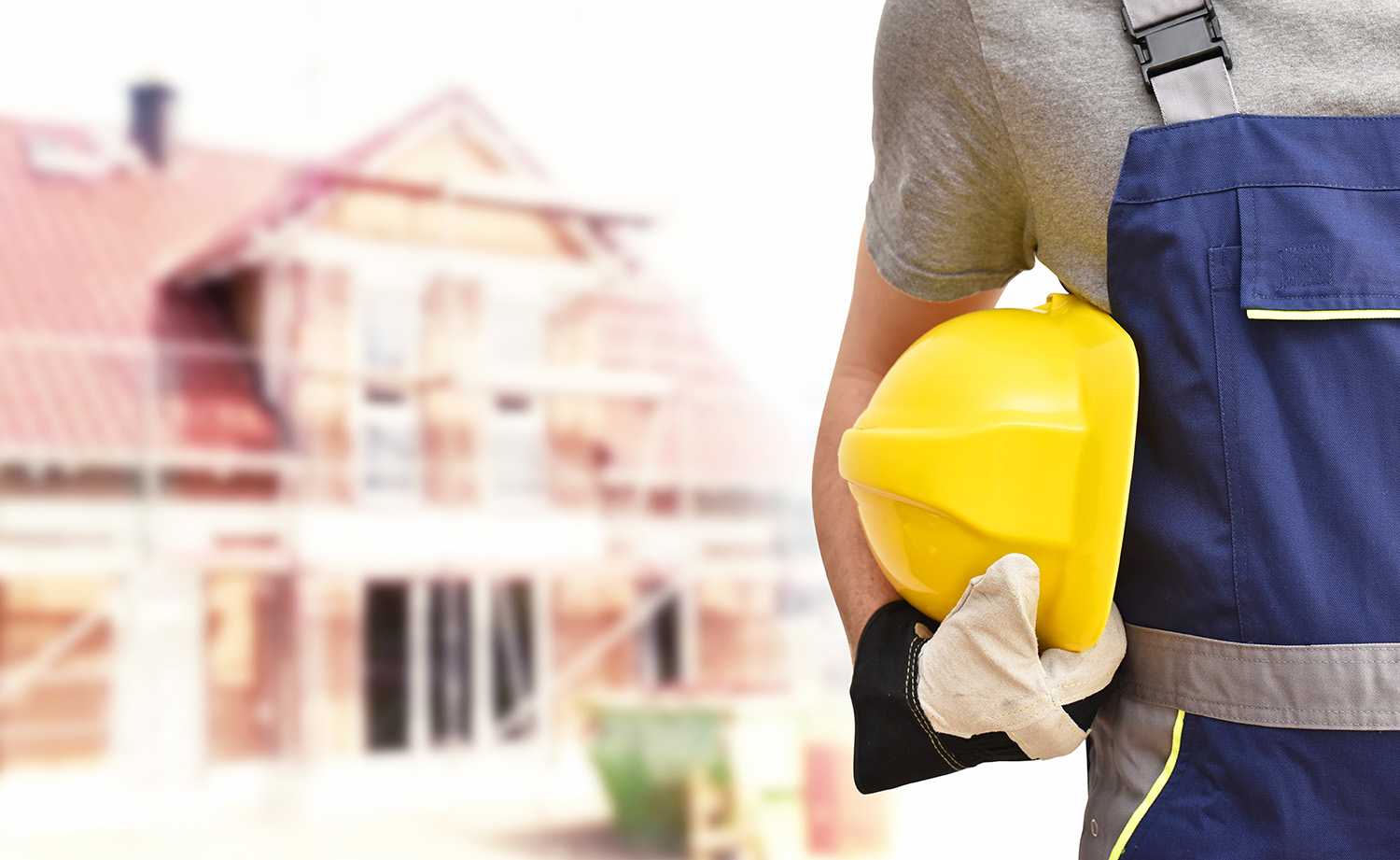 Bauarbeiter mit Helm und Haus im Rohbau im Hintergrund