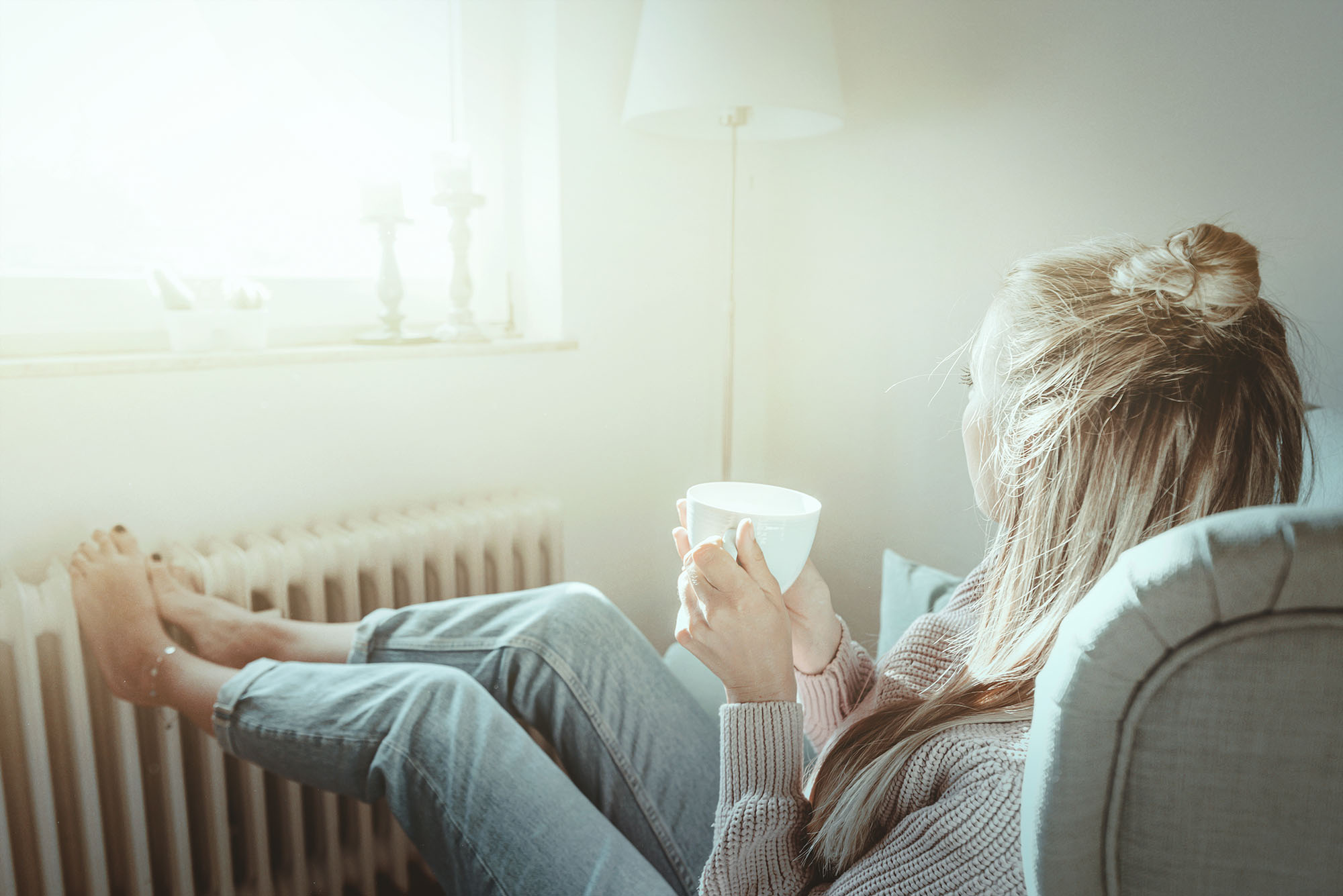 Frau macht es sich an wärmender Heizung mit Kaffee gemütlich